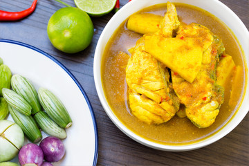 Yellow curry with Snapper fish and coconut shoot in white bowl on wooden table Thai food delicious