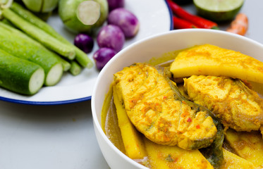 Yellow curry with Snapper fish and coconut shoot in white bowl on wooden table Thai food