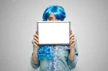 Christmas congratulatory letter. Special offer. Happy girl with blue hair holds in hands a blank empty photo frame with copy space.