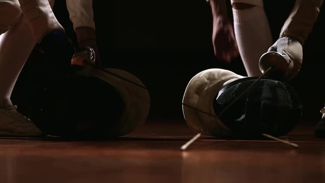 Closeup on the floor on the mask and rapier for fencing. A man and a woman come and pick them up.