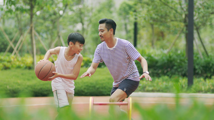 Asian father & son playing basketball in garden in morning