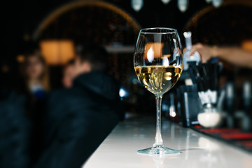 A glass of white wine close-up on a bar, white counter. Dark background.