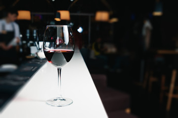 A glass of red wine close-up on a bar, white counter. Dark background.