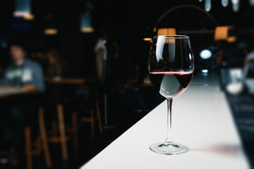 A glass of red wine close-up on a bar, white counter. Dark background.