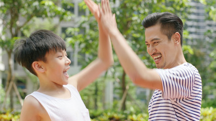 Asian father & son giving a high five after scoring outdoors in morning