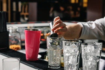 Male hands of the bartender close-up, makes a cocktail on the bar, glasses with ice.