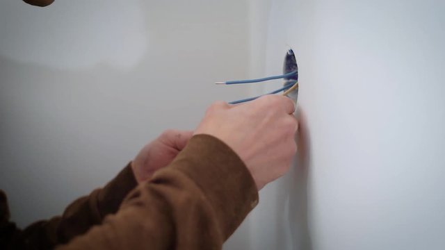 wireman is connecting wires to a mechanism of electric outlet during repair indoors, using a turn-screw
