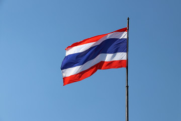 Thai national flag in blue white and red color on the flagstaff blowing with the wind on blue sky background. National flag of Thailand, three color on the fabric.