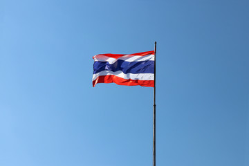 Thai national flag in blue white and red color on the flagstaff blowing with the wind on blue sky background. National flag of Thailand, three color on the fabric.