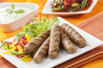 Chicken Seekh Kebabs with letus coloured bell pepper with tomato onion pickle and yogurt herb dip on white plates and on orange background