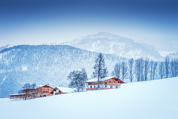 Winter landscape at early morning in Austria with snow, wooden buildings, blue sky and copy space