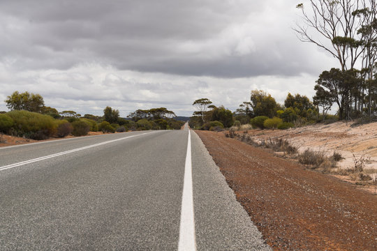 Leere Straße mit rotem Sand auf dem Seitenstreifen im Outback von West-Australien
