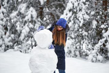 Fototapeta na wymiar winter fun. girl in a knitted hat sculpts a snowman.