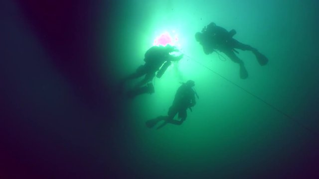Silhouettes of technical divers passing decompression on the background of a water surface, a solar disk and a diveboat.
