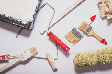 Used painting tools with red handles covered in warm white paint layed out in a composition on a...