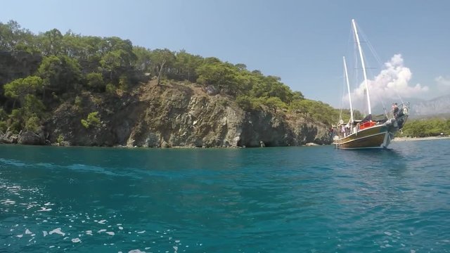 An impressive two-mast brigantine standing at anchor at a hilly Turkish seacoast on a sunny day in summer in slow motion. It looks fine. 