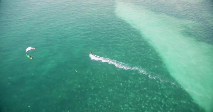 Aerial view of Kitesurfer cruising on empty blue water lagoon on tropical island