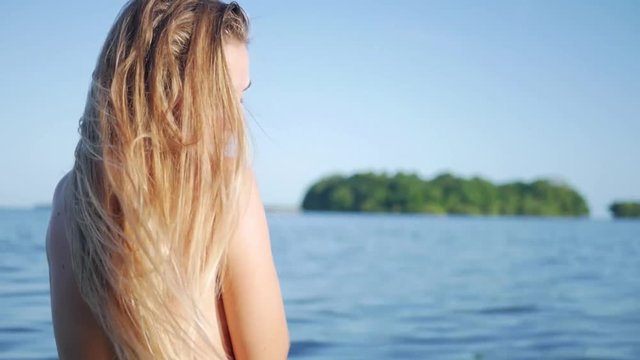 Bokeh shot Topless blond girl from the back walking in water looking at horizon