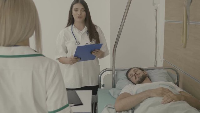 Nurses talking to each other while a patient is on the bed