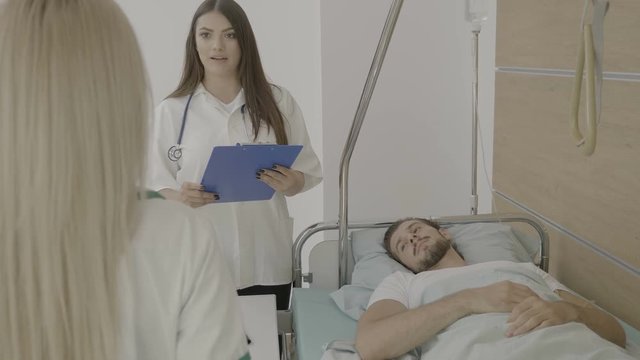Two nurses with folder in hands talking to each other while a patient is on the bed