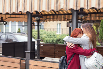 Two female teenagers embracing at the city street cafe