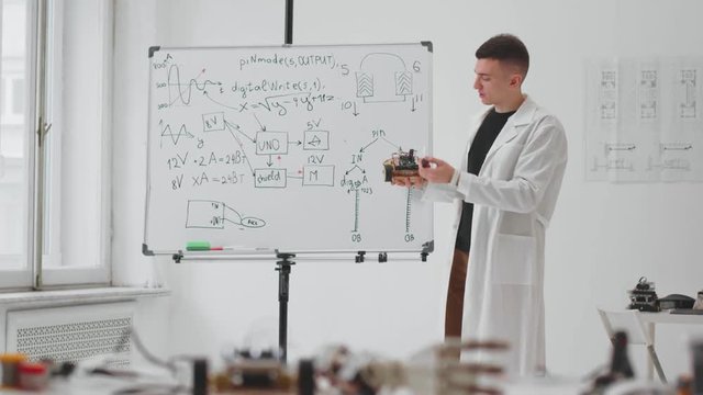 Young technician engineer holding in hand new invention and showing formulas