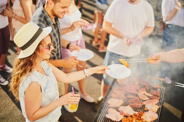 Group of people standing around grill, chatting, drinking and eating. - obrazy, fototapety, plakaty