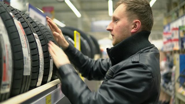 Young man looking over automobile tyres in the automotive department of the hypermarket and trying to choose