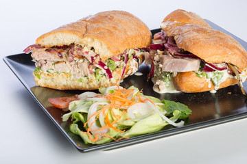 Close up of tuna sandwich with vegetables on a black plate isolated