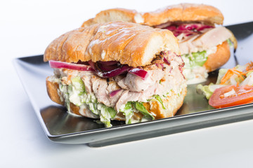 Close up of tuna sandwich with vegetables on a black plate isolated