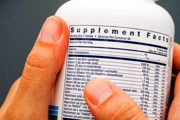 White plastic jar with supplement facts of multivitamins in person hands. - obrazy, fototapety, plakaty