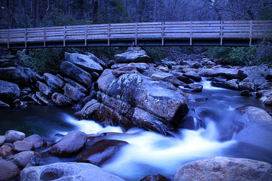 Slow Shutter Speed River Photography of a Small Waterfall with a Wooden Walk Way Bridge over the River.