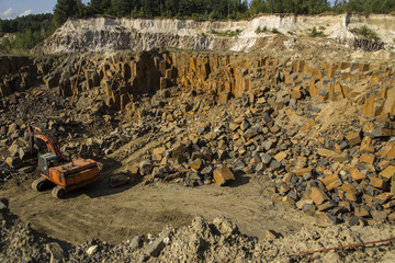 Excavator and basalt columns rocks. Heavy industry. Stone excavation. Producing stone from basalt...