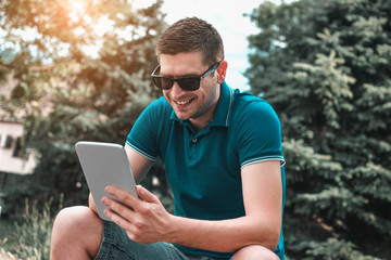 Young man using tablet on park bench on a summers day