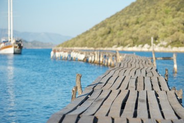 Obraz premium An amazing picture of a wooden pier going into the sea with a boat coming towards it and beautiful green hills in background. 