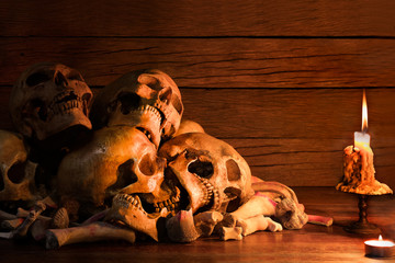 Pile of skulls and bone put on the wooden table which has bright candle light by candle flame.Still life image and art visual with selective focus.