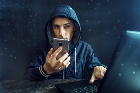 Male Hacker Uses The Mobile Phone To Hack The System. Concept Of Cyber Crime And Hacking Electronic Devices