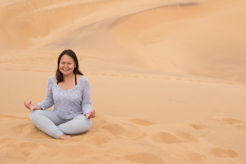 Fototapeta na wymiar Indonesian girl in lotus posture on Dune 7, Walvis Bay, Namibia