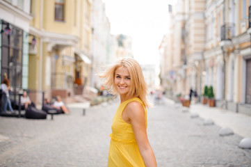Fototapeta premium Beautiful blonde woman dressed in a yellow dress walking around the city