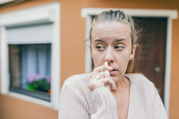 Woman is having flu and she is using nasal spray to help herself. Woman using nasal spray