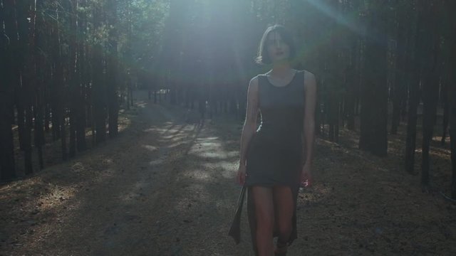 Shapely brunette walks in the woods. Shooting for the fashion industry. Attractive model in bodycon dress walks in the forest on sunny day. Model going on the camera.
