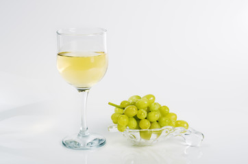 Glass of white wine and a bunch of green grapes on a glass plate, on a white background