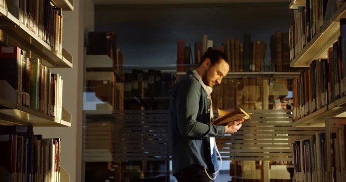 The library passage with books shelves and attractive young man passing the passage while reading a book and holding it. Inside