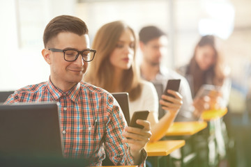Group of university students sitting in a row and using computers and mobile phones in the classroom