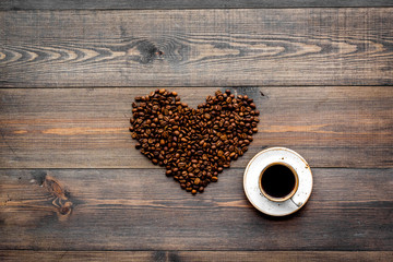 Cup of freshly brewed full-bodied coffee near beans in heart shape on dark wooden table top view copyspace. Coffee background.