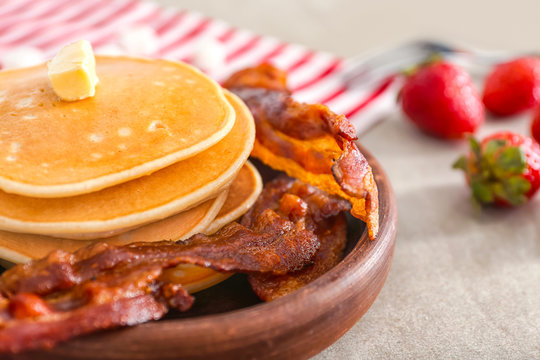Wooden plate with pancakes and bacon on table, closeup