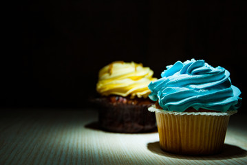 Yummy cupcake with buttercream on wooden table against dark background with copy space.