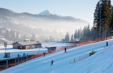 Shot of a skiers skiing down the hill on a beautiful sunny morning. The snow-white scenery of mountains and forests and haze over it. Ski resort Bukovel in the Carpathians nature
