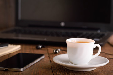 Cup of coffee on a laptop keyboard. Work place modern. Laptop (notebook) with cup of coffee and notepad with pen on old wooden table.