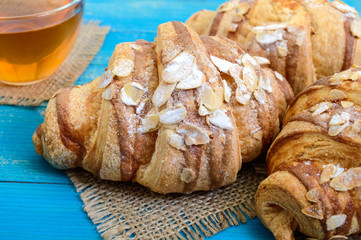 Freshly baked croissants with almond flakes,  cup of tea on a blue wooden background. French pastries. Breakfast.